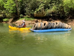 a kayaker hauls a blue ducky boat full of tires down the river