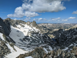 a snow-strewn, sunny view from the top of rugged mountain peaks