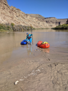 A person struggles to walk through mud, pulling a small raft along in a few inches of water