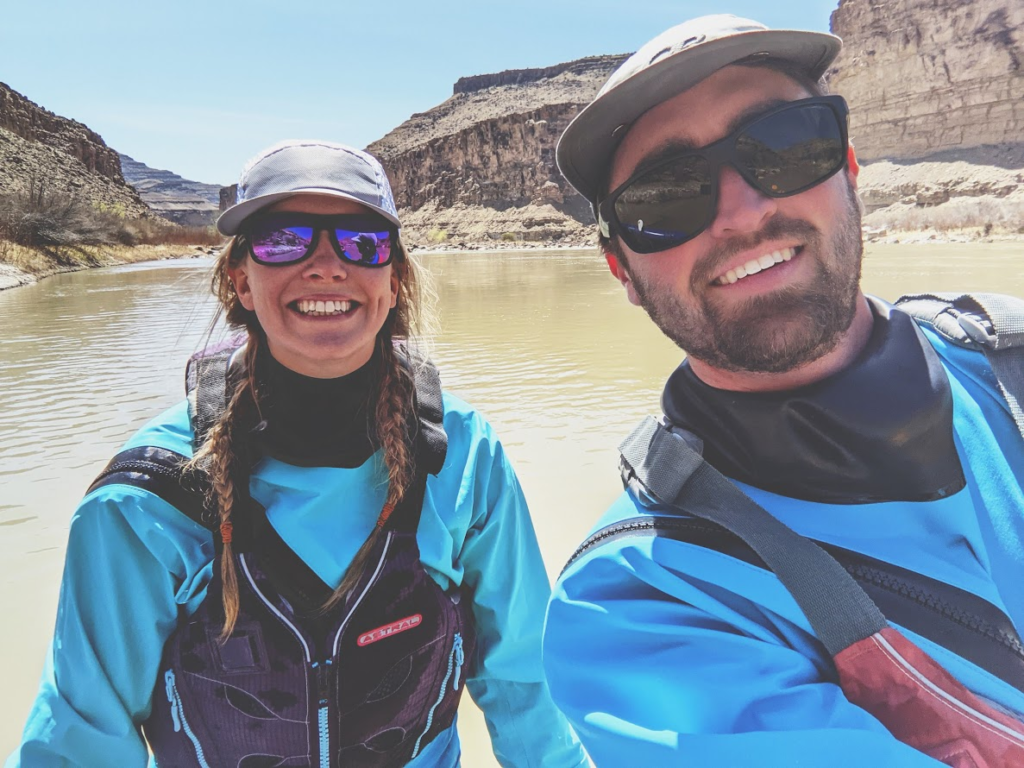 Two people in rafting gear and sunglasses smile for a selfie