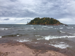 a stormy sky hangs over white-capped waves breaking on the shore. An island dominates the horizon