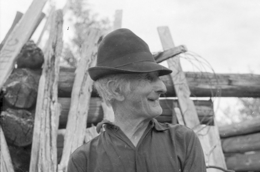 Black-and-white photograph of George F. Wright in a felt hat in front of a log structure