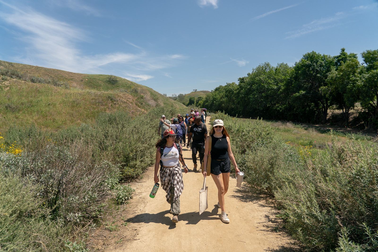 A group of volunteers walks a dirt trail through green hills on a sunny day.